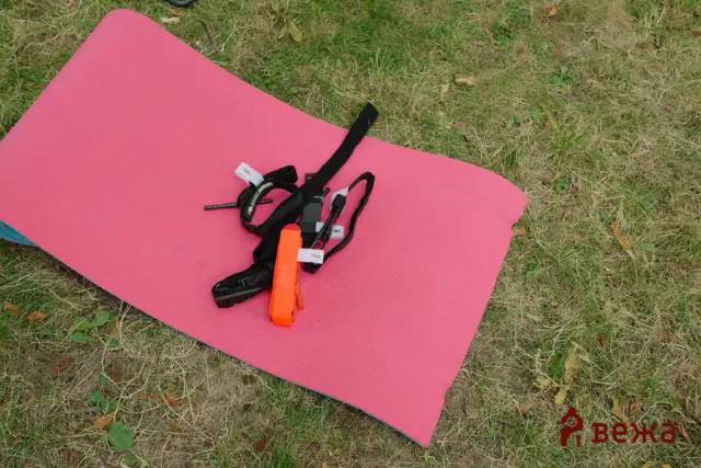 Pink yoga mat on grass with a black climbing harness and orange safety gear resting on it.