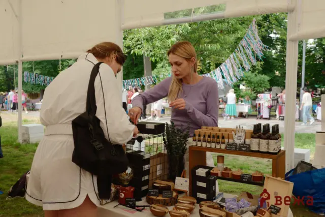 Two women at an outdoor market stall examining skincare products displayed on a table under a white canopy.