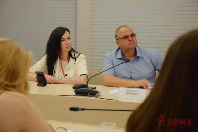 Panel discussion with a woman on the left and a man on the right seated at a conference table; nameplate reads Микола ФРАНКО in front of him.