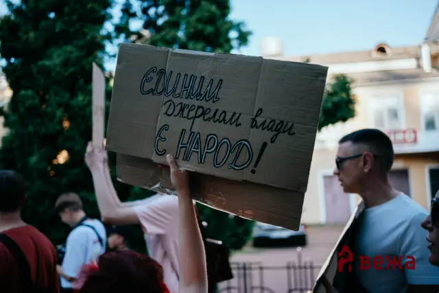 Protester raises a cardboard sign with handwritten Cyrillic text during a street demonstration.
