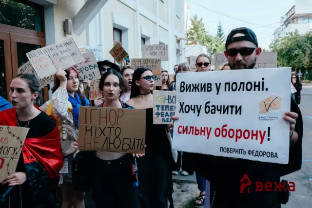 A group of protesters holding handwritten cardboard signs in Ukrainian on a city street during a demonstration.