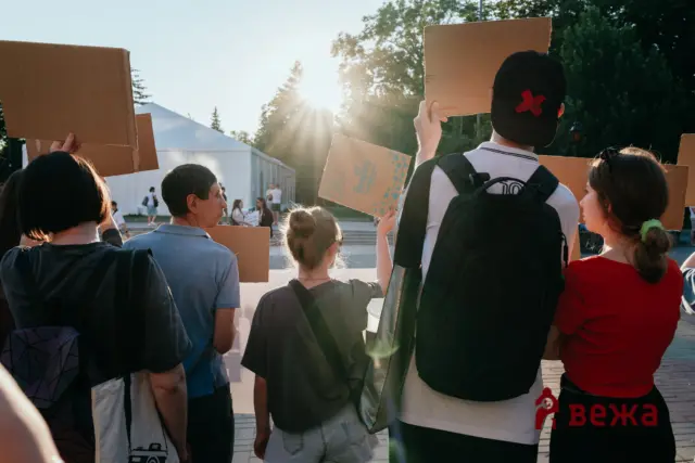 Group of protesters seen from behind, holding cardboard signs outdoors at sunset during a demonstration